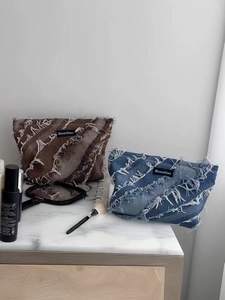 Close-up of denim toiletry bag with frayed edges and Moonshine label on marble surface