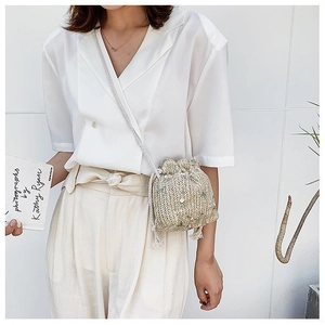Détail d'un sac seau en paille beige avec cordon de serrage et bandoulière tissée