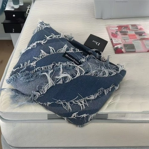 Blue denim fringe toiletry bag with Moonshine label placed on a bed surface