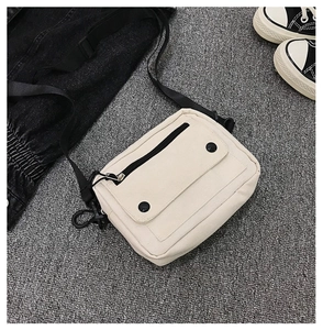 Flat lay showing details of a cream canvas crossbody bag with black buckles and straps