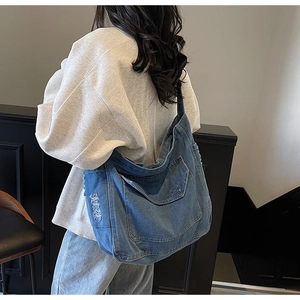 Détail du grand sac hobo en jean bleu avec bords effilochés et vue de la poche latérale