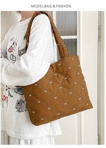 Detail of a brown quilted tote bag with white bow embroidery and padded shoulder straps