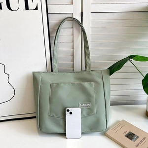 Light green nylon tote bag with front pocket showing large capacity next to a smartphone