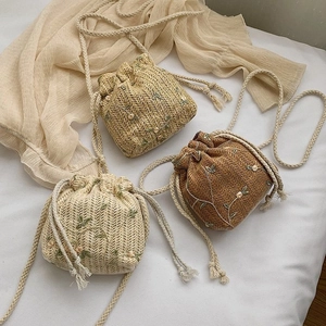 Vue détaillée des sacs seaux en paille tressée avec broderies florales et cordon