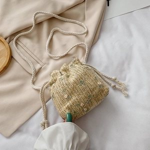 Détail du sac seau en paille beige avec broderie florale et cordon de serrage en coton