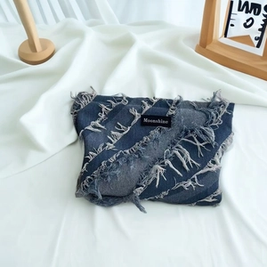 Detailed close-up of dark blue denim toiletry bag with fringe texture and logo