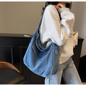 Gros plan sur le sac bandoulière en jean bleu vintage avec coutures blanches et texture lavée