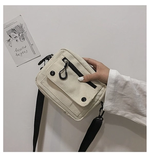 Close-up of minimalist white canvas crossbody bag with black contrast zipper and buckle detail