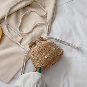 Détail de broderie florale sur sac seau en paille avec cordon de serrage