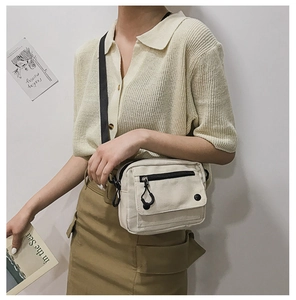 Detail view of beige canvas crossbody bag with adjustable black strap on a female model