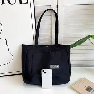 Detail of a black nylon tote bag with a silver FASHION label and large exterior pocket