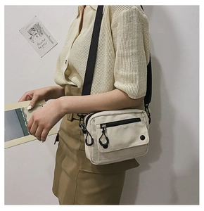 Detail of off-white canvas crossbody bag with adjustable black strap and front pocket