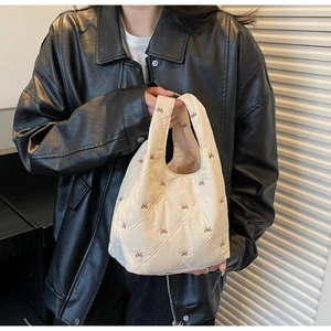 Detail of cream quilted handbag with bow prints shown on a black leather jacket