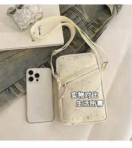 Mini cream crossbody phone bag with silver stars shown next to a smartphone for size reference