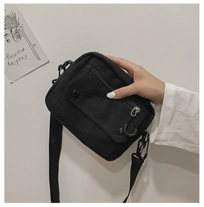 Close-up of black canvas crossbody bag with adjustable nylon strap and button pocket