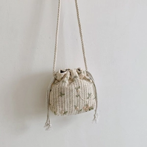 Détail du sac seau en paille beige avec broderies florales et fermeture à cordon