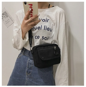 Detail of black canvas crossbody bag with zipper front pocket and adjustable nylon strap