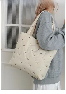 Detail of white quilted tote bag with brown bow embroidery shown on a model