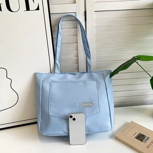 Detail of light blue nylon tote bag with front pocket and fashion label on a white table