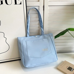 Close-up of a light blue nylon tote bag with fashion label and front pocket detail