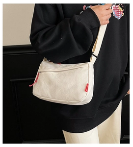 Detail of cream nylon crossbody bag with red zipper puller and fashion label on model