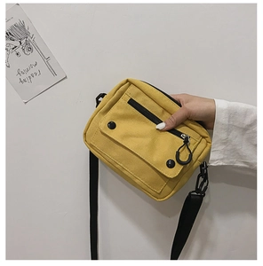 Detail view of yellow canvas crossbody bag featuring adjustable black strap and zippers