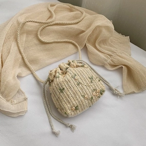 Détail du sac seau en paille tissé à la main avec broderie florale et bandoulière corde