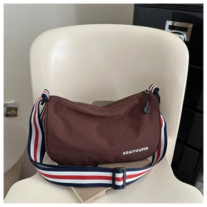Dettaglio di una borsa a tracolla in tela marrone con ampia tracolla a righe colorate