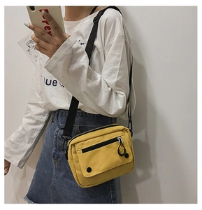 Detail of yellow canvas crossbody bag with adjustable strap and metal buckles shown on model