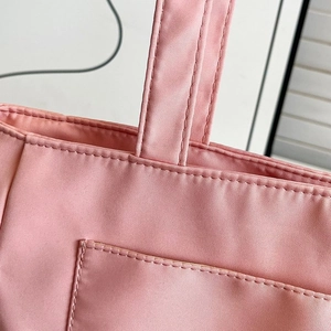 Detail of light pink nylon tote bag showing double-stitched reinforced handles and fine texture
