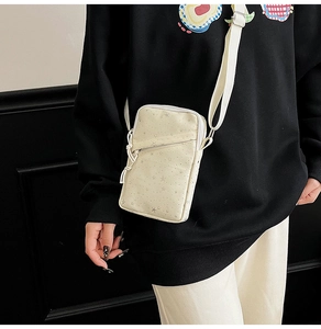 Detail of off-white canvas crossbody phone bag with silver star print and adjustable strap