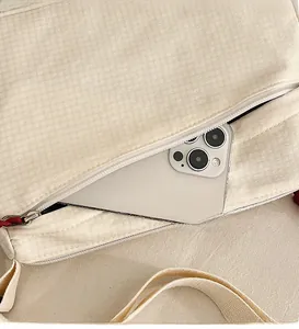 Detail of front zipper pocket on beige textured nylon crossbody bag showing phone storage