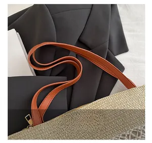 Détail du cabas en paille tissée avec anses en cuir marron et fermeture éclair dorée