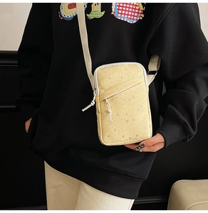 Yellow crossbody phone bag with silver star prints on shoulder of a model in hoodie