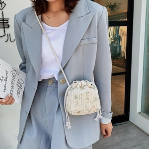 Détail d'un sac seau en paille avec broderie florale et bandoulière en coton blanc