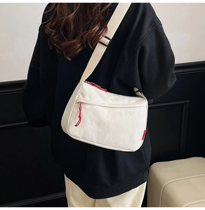 Detail of a white nylon crossbody bag with red zipper pull on a casual shoulder strap