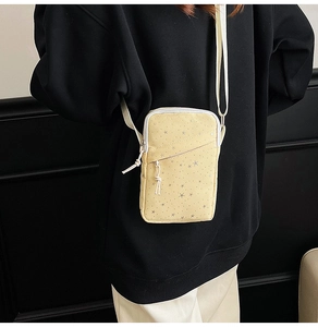Detail of yellow crossbody phone bag with star pattern worn on back over black background