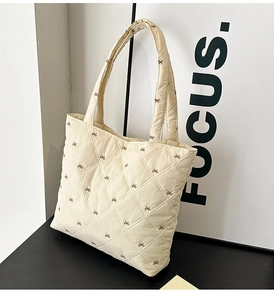 Detail of cream quilted tote bag showing embroidered brown bows and diamond stitching