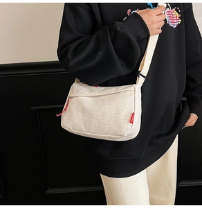Detail of white nylon crossbody bag with grid texture and red zipper pull on black hoodie