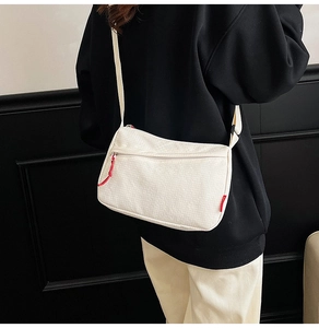 Detail of white nylon crossbody bag featuring red zipper pulls and textured fabric
