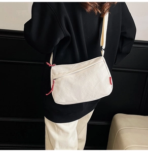Detail view of cream-white nylon crossbody bag with zipper pockets and red accents