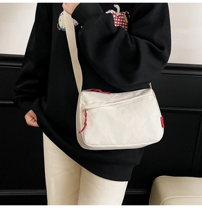 Detail of beige corduroy crossbody bag with red fashion label and woven zipper puller