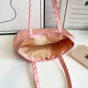 Detail view of the silver magnetic buckle closure and yellow lining of the pink nylon tote