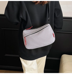 Detail view of grey nylon crossbody bag with square texture and red zipper pulls