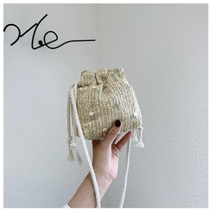 Détail d'un sac seau en paille avec broderie florale rose et bandoulière en corde