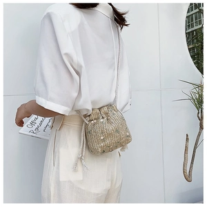 Détail d'un sac seau en paille avec fermeture à cordon et bandoulière en corde blanche