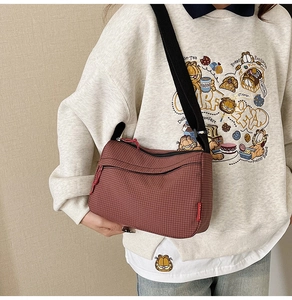 Detail view of reddish-brown plaid nylon crossbody bag with fashion label and zipper