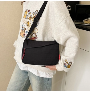 Detail of black nylon crossbody bag featuring a red zipper pull and a fashion side label