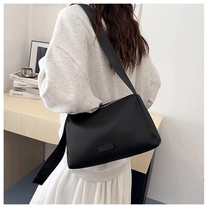 Detail view of a black minimalist crossbody bag with wide nylon strap on a model