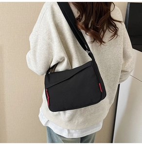 Detail view of black nylon crossbody bag featuring red cord zipper and adjustable strap